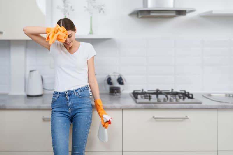 a women standing in the kitchen while holding a spray bottle using a DIY cleaning