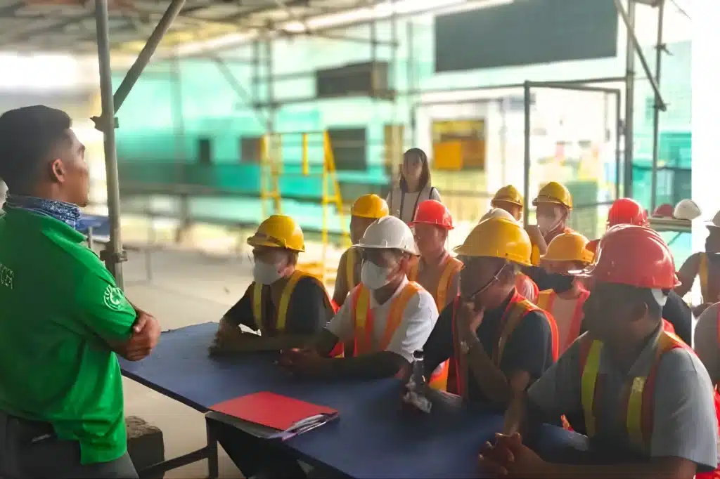 A group of people seated, attentively listening to a male instructor on what to do during earthquake drills.