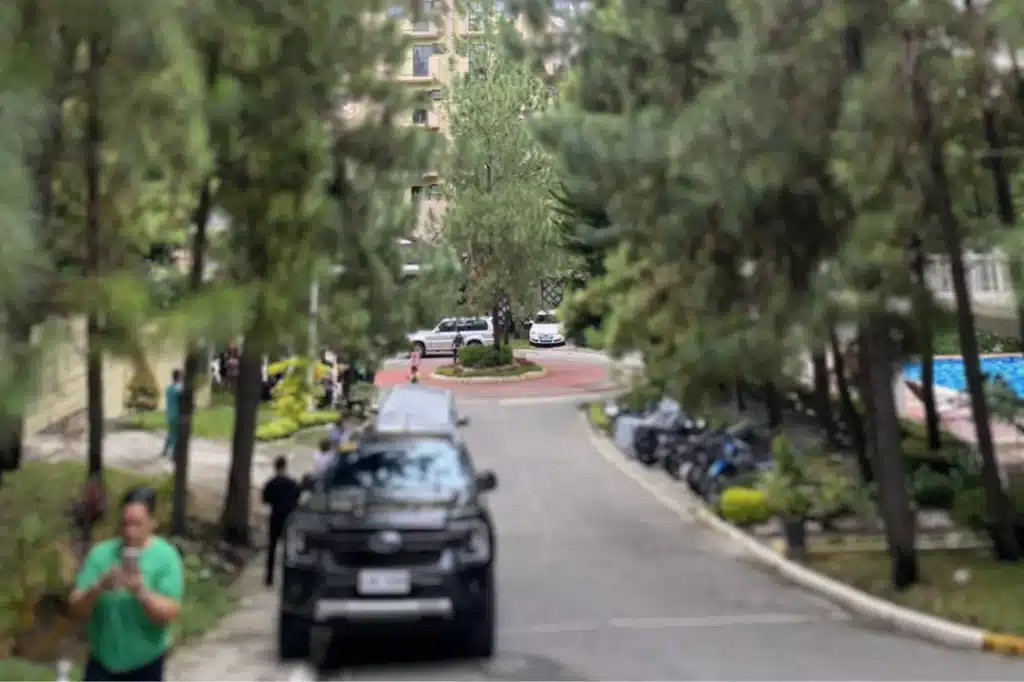 people outside of the building, surrounded by trees and parked vehicles.
