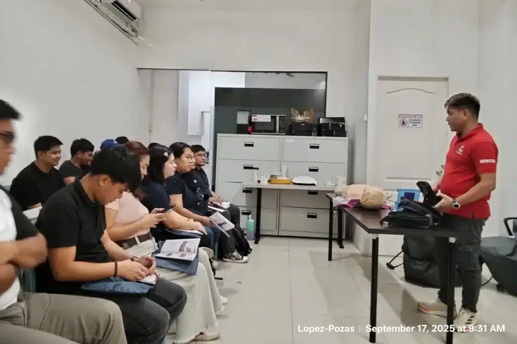A group of people seated in a classroom setting attentively listening to a male instructor in a red shirt